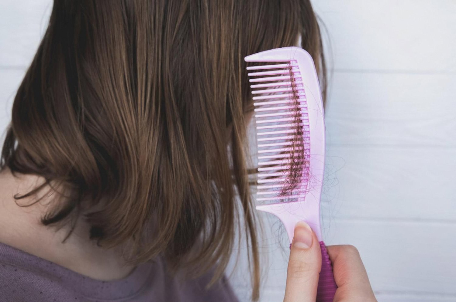 Woman finding clumps of hair in a pink comb, a common sign of hair loss